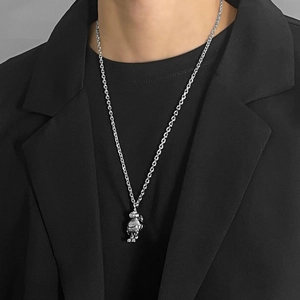 Close-up of a silver astronaut robot pendant on a steel chain over a black suit