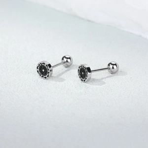 Detailed macro of silver stainless steel barbell earrings with sunburst and scroll pattern