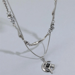 Détail du collier argenté à deux rangs avec pendentifs lune et étoile et zircon noir