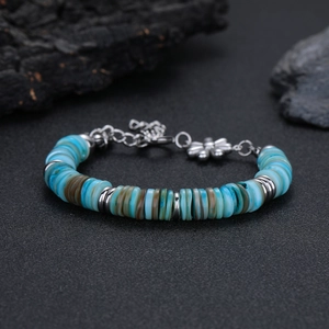 Dettaglio del bracciale con perline blu e ciondolo a fiore su roccia scura e strutturata
