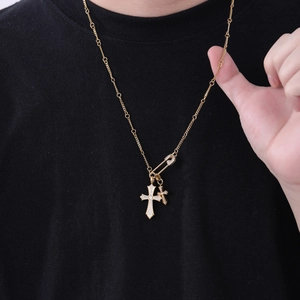 Detail der goldenen Halskette mit Doppelkreuz und Sicherheitsnadel mit glänzenden Steinen