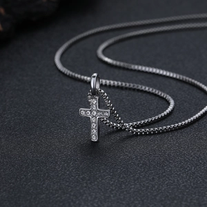 Vista macro di collana con croce in titanio argento e zirconi con catena box