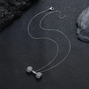 Détail d'un pendentif haltère argenté serti de strass blancs sur une surface noire mate