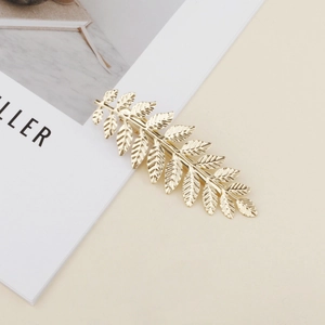 Elegant gold leaf metal hair clip with detailed leaf texture on a minimalist beige background