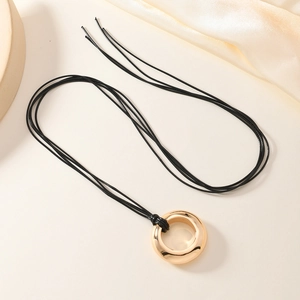 Collier minimaliste avec pendentif cercle doré et cordon noir sur fond de soie douce