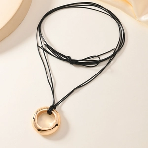 Collier minimaliste avec pendentif anneau doré et cordon noir sur fond beige élégant