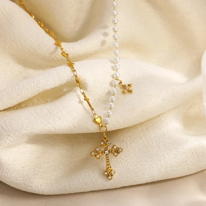 Stainless steel gold cross necklace with pearls and heart charms on fabric background