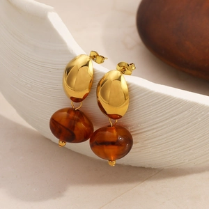 Gold-plated drop earrings with amber resin beads hanging on white textured ceramic