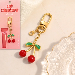 Detailed close-up of a cherry-shaped golden keychain with green leaves and red beads