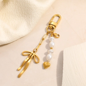 Detailed view of a gold-plated bow charm with pearl beads and a heart pendant for bags
