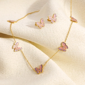 Makroaufnahme von 18K Gold Schmetterling Schmuckset mit rosa Glitzer auf beigem Stoff
