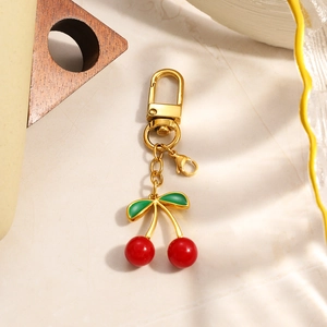 Golden cherry pendant keychain with red beads and green leaves on stone background