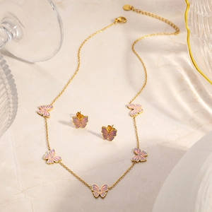 Detail von 18K vergoldetem Schmetterling-Schmuckset auf Marmorplatte mit Glasgeschirr