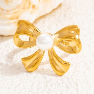 Polished 18K gold plated bow ring with center pearl on textured background