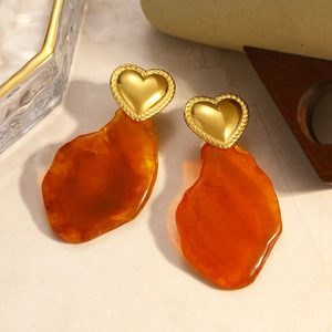 Detail view of heart-shaped 18K gold earrings with amber resin stones on stone prop