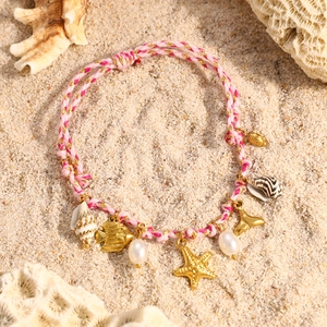 Detalle de una pulsera oceánica tejida rosa con colgantes de oro de 18K en la arena