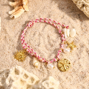 Detalle de pulsera trenzada oceánica con conchas y dijes sobre arena de playa