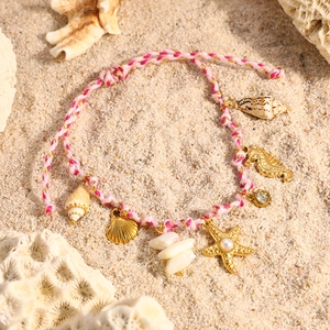 Primer plano detallado de pulsera trenzada oceánica con dijes de conchas en arena de playa