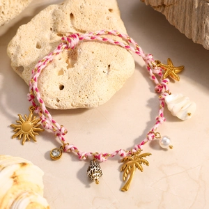 Detalle de pulsera tejida rosa con dijes dorados de palmeras, estrellas y caracoles