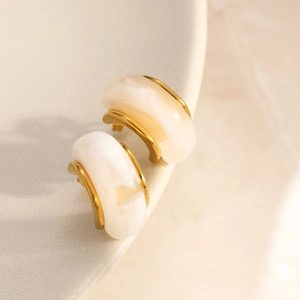 Detailed macro view of C-shaped 18K gold earrings with translucent resin inlay on ceramics