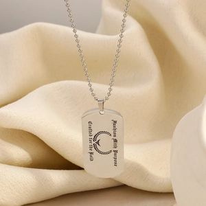 Stainless steel dog tag necklace with engraved eagle logo on a beige fabric background