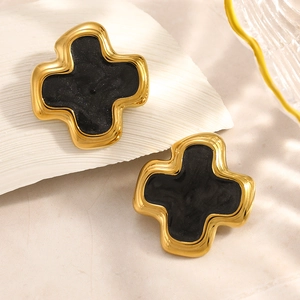 Détail de boucles d'oreilles croix dorées avec émail noir et fini scintillant sur fond blanc