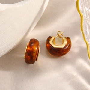 Dettaglio di orecchini a C in resina ambra con placcatura in oro 18K su marmo elegante