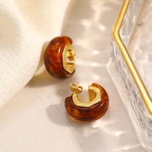 Orecchini a C in resina ambrata con inserto esagonale in oro 18K su superficie in pietra