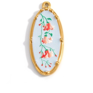 Macro shot of oval gold-plated pendant with vintage blue base and pink flower embroidery
