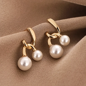 Elegant gold geometric earrings with pearls on dark brown satin background