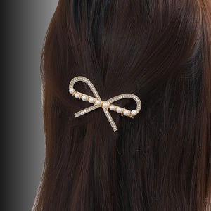 Elegant gold bow hair clip with pearls and rhinestones on dark hair, stylish fashion accessory