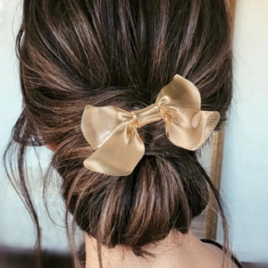 Elegant gold bow hair clip with brushed metal texture on a classic low bun hairstyle