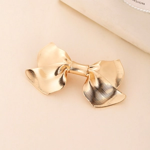 Close-up of golden metal bow hair clip showing elegant vertical brushed texture and shine