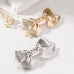 Elegant gold and silver metallic bow hair clips with minimalist striped texture on off-white surface