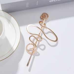 Épingle à cheveux en métal doré au design torsadé irrégulier sur un bureau blanc