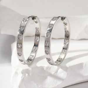 Sparkling silver hoop earrings with diamond-set hearts on a minimalist textured stone base