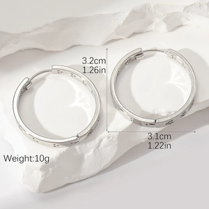 Detailed view of silver hoop earrings with star-pattern engraving on a white stone base