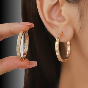 Detailed view of gold hoop earrings with sparkling diamond heart charms on a model