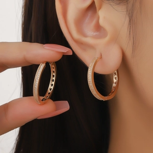 Detailed close-up of golden hoop earrings with pavé zircons and heart hollow pattern