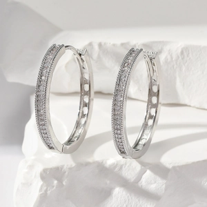 Close-up of silver hoop earrings with white zircons on a white textured stone base