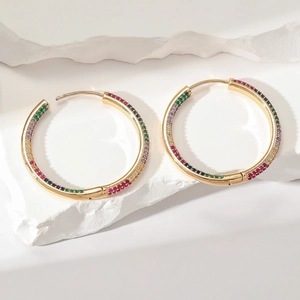Macro detail of large gold hoop earrings with multi-color zircon stones on white stone base