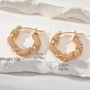 Détail de boucles d'oreilles créoles torsadées dorées avec pavé de zircons et mesures