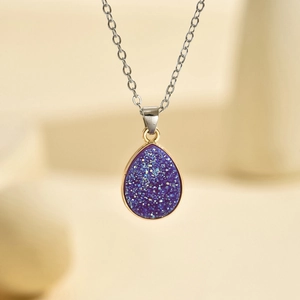 Macro d'un pendentif goutte d'eau en résine pailletée violette avec lunette dorée et chaîne