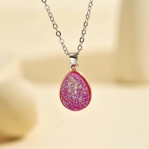 Macro d'un pendentif goutte en druzy fuchsia avec bordure dorée sur chaîne argentée