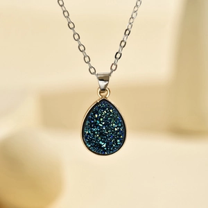Vue macro du pendentif goutte druzy bleu avec bordure dorée et chaîne argentée