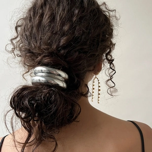 Polished silver metal hair ring and gold U-shaped beaded earrings on elegant wavy hair
