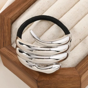 Sleek silver metal spiral ponytail holder on black elastic band displayed in a wooden box