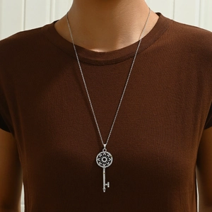 Elegante collana lunga d'argento con ciondolo a chiave con strass su un top in maglia marrone