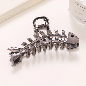 Detail shot of a dark gunmetal fishbone hair claw clip with crystal eye on a cream surface
