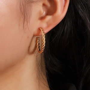 Gros plan de boucles d'oreilles créoles dorées en forme de C torsadé sur un modèle féminin